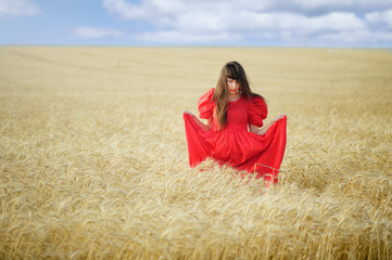 Woman in a wheat field in a red long dress, holds in hands.