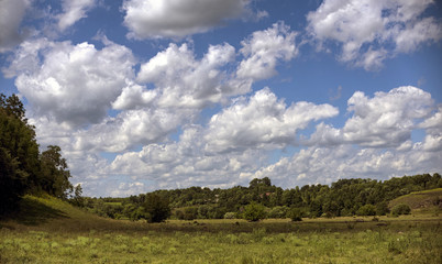 Fototapeta premium Floating in the blue sky, large clouds over the meadow.