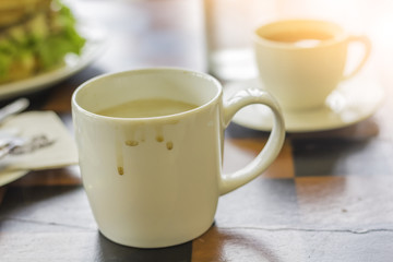 White coffee mug and white tea mug put on a brown wooden table in the morning cafe.