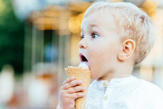 Sweet toddler boy eating ice cream over background with blurred carousel and bokeh