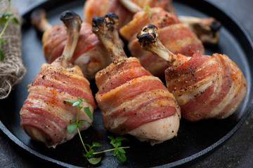 Close-up of oven-baked chicken legs wrapped in bacon, selective focus, horizontal shot