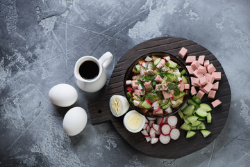 Black wooden serving board with russian okroshka or cold soup with kvass, above view on a grey stone background
