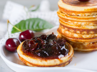 Homemade American pancakes served with cherry jam and fresh cherry on a wooden background