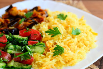 Vegetable rice, eggplant ragu, tomatoes and cucumber salad on a white plate and a brown wooden table. Healthy and delicious vegetarian recipe idea. Closeup