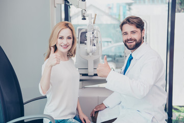 Obraz premium Healthcare, people, eyesight and vision concept. Smiling man optician in white coat and a blond woman patient are showing thumbs up gesture at optics store