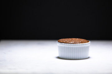 Chocolate creme brulee before caramelization, in a ramekin on white marble against a black background