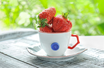 Strawberries in a white decorative Cup on the green blurred background.