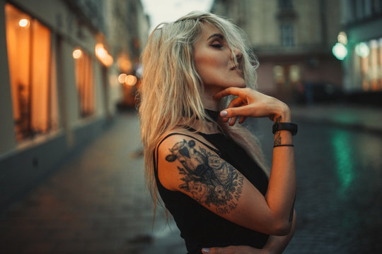 Young woman portrait with tattoo on shoulder standing on city street in evening.