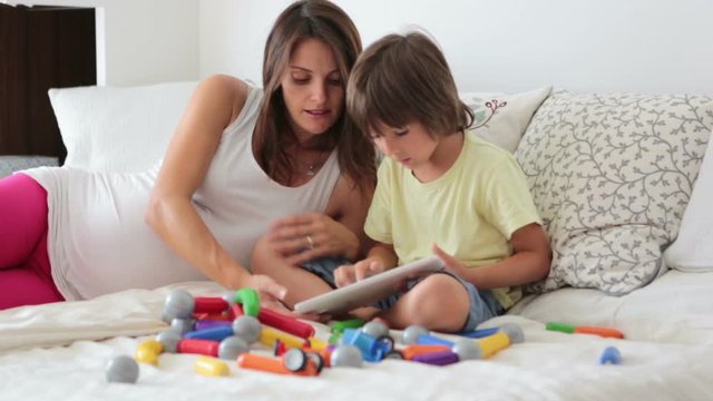 Cute pregnant mother and child boy playing together indoors