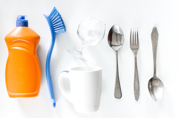 Dishwashing liquid, tableware and brushes on white background top view