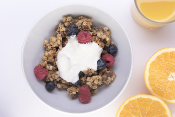 Bowl of granola filled with blueberries and raspberries covered with yogurt, with a glass of orange juice 