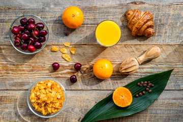 Light summer breakfast. Muesli, oranges, cherry, croissant and coffee on wooden table background top view