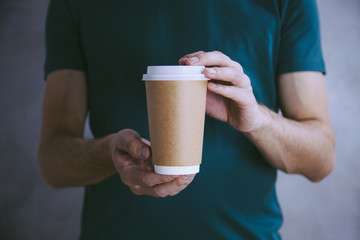 Hands holding a paper coffee cup to take away on green t-shirt background. Mock up, perfect for...