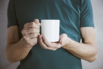 Man in green t-shirt holding big white coffee cup.Mock up of clean coffee cup.Horizontal mockup.
