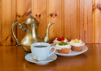 Fototapeta na wymiar Cup of coffee, sweet cakes with fruits and coffee pot on wooden table