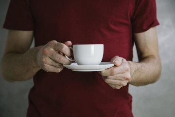 Young man in red t-shirt holding white cup in hands. White mug for man, gift. Mockup for designs.