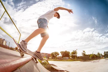 Zelfklevend Fotobehang Teenager skater in a cap and shorts on rails on a skateboard in a skate park © yanik88