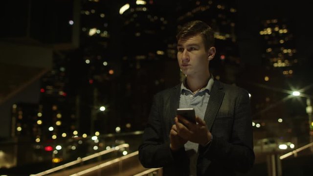 Handsome young student is using his smartphone for social networks while standing on a street