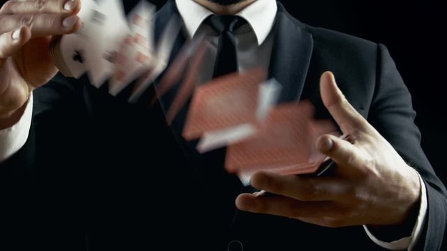 Close-up of a Suited Magician's Hands Performing Card Trick. Throwing and Catching Cards in the Air. Background is Black. Sleight of Hand. Slow Motion. Shot on RED EPIC-W 8K Helium Cinema Camera.