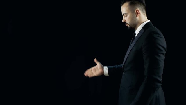 Professional Skilled Magician in a Black Suit Performs Card Disappearance and Appearance Trick Multiple Times. Background is Black. Shot on RED EPIC-W 8K Helium Cinema Camera.