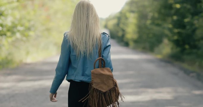 Woman walking away on a countryside road, back view