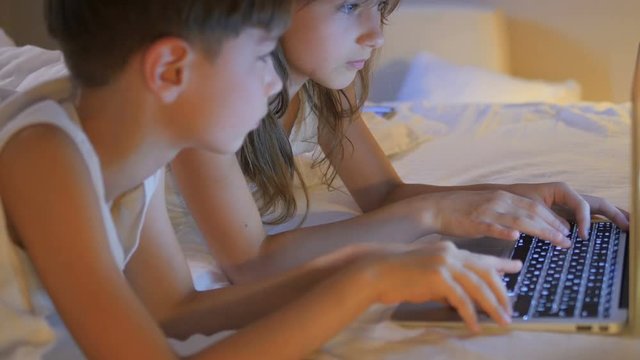 Children play on the computer in the bed under the blanket at night. Computer games.