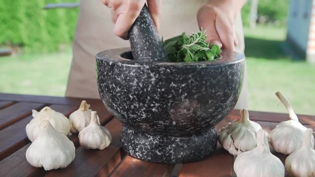 Housewife grinds garlic and parsley for spicy natural sauce outside, cooking food, spicy food, vegetarian meal, greens and salads