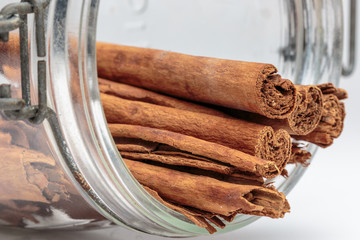 Cinnamon sticks come out of overturned glass jar, on white