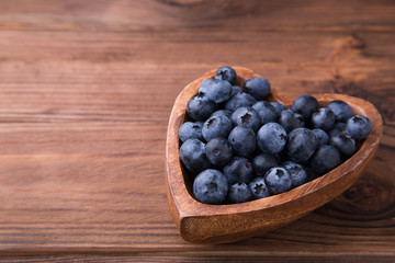 Wooden bowl in the shape of heart with blueberries standing on brown rustic background. Healthy food