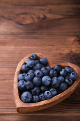Wooden bowl in the shape of heart with blueberries standing on brown rustic background. Healthy food