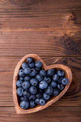 Wooden bowl in the shape of heart with blueberries standing on brown rustic background. Healthy food