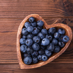 Wooden bowl in the shape of heart with blueberries standing on brown rustic background. Healthy food