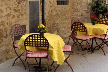 Traditional restaurant in Pienza, Tuscany Italiya. Tables with beautiful yellow tablecloths, vintage chairs and flowers.