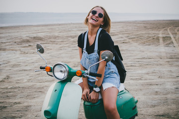 Young female laughing while sitting on retro scooter on the beach - 164211923