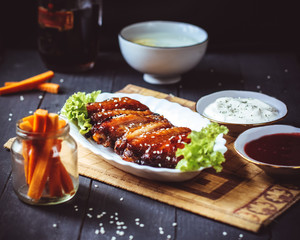 Fried chicken wings with carrots, spicy berry sauce, tartar sauce, greens and a mug of dark beer over a gray wooden background