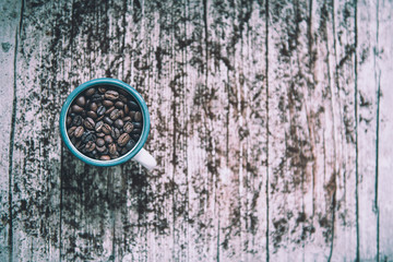 Cup of porcelain with coffee beans in foreground in vintage style.