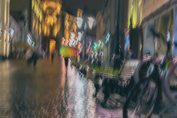 Abstract blurred background of girl under colorful vivid umbrella, city street in rain. Light...