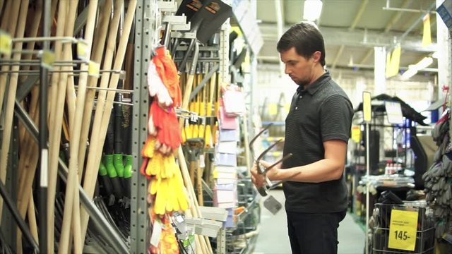 Modern farmer in the mall looking for big garden forks for his farm. He taking one of the forks and trying it in hands