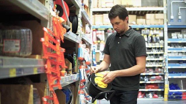 Young male customer in the mall choosing an electric wire extension cord with a long cable.