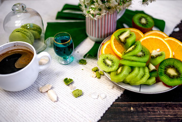 Morning tea or coffee with orange and kiwies slices and green macaroons on a white blanket with cherry blossom