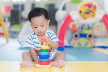 Adorable Asian baby boy 9 months sitting and playing with color developmental toys in kids room at home..