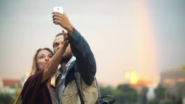 Young happy couple walking on sunset and taking the selfie photos. Smiling man and woman use smartphone.