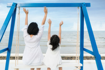 Happy Asian family Mother with child having fun swinging near sea. Summer vacation travel and holiday family concept.