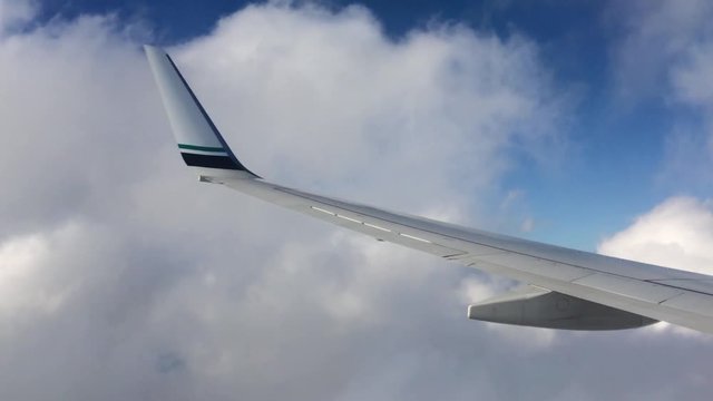 Wing of an airplane flying above the clouds. People look at the sky from the window of the plane, using air transport to travel