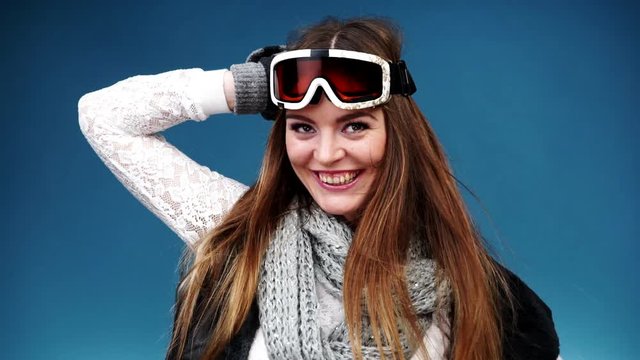 Woman smiling skier girl wearing warm clothing ski goggles portrait. Winter sport activity. Beautiful long hair sportswoman on blue studio shot, full HD.