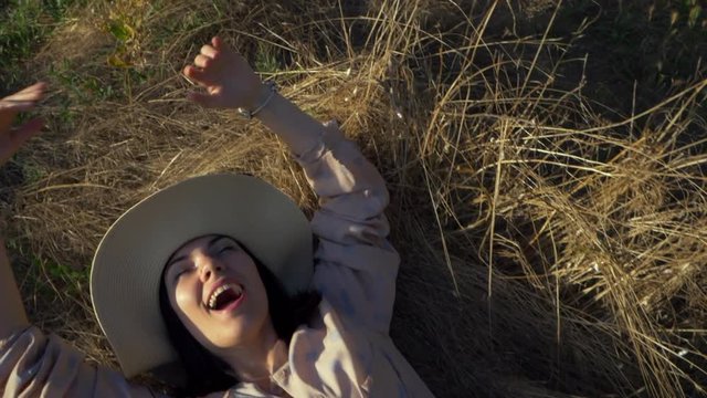 Beauty Girl with summer cowboy hat Outdoors. Happy Smiling Young Woman falling down on the yellow grass. Beautiful young woman lying on the field. Enjoying Nature. Slow motion video footage.