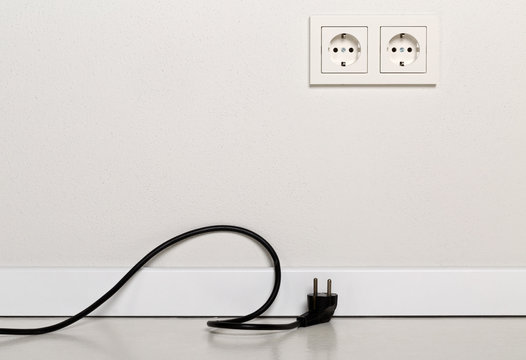 Black power cord cable unplugged with european wall outlet on white plaster wall