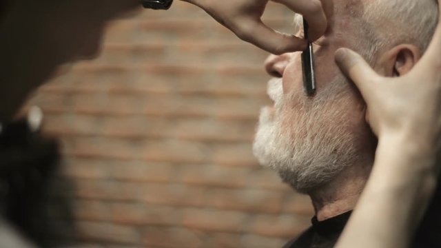 Active retired elderly old bearded senior man aged with graying hair in barber shop hairstylist hairstyle getting Haircut and shaving , head, beard and mustache