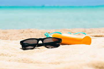 Fototapeta na wymiar Sunglasses, Sunscreen Lotion And Slippers On The Beach