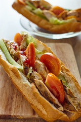 French bread sandwich with chicken and vegetables on the wooden table